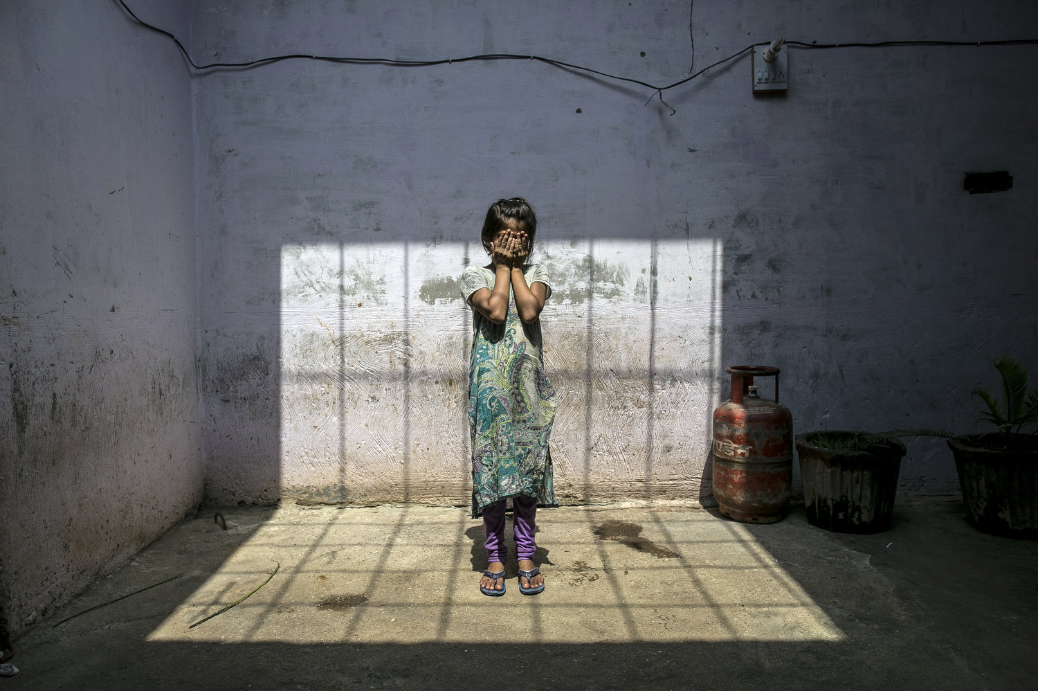 UTTAR PRADESH, INDIA - SEPTEMBER 8:  8 year old Sadaf (name changed) stands for a photo in her home September 8, 2016 in Uttar Pradesh, India. 3 months ago she was raped by a doctor in her village. She was walking to the market to buy sweets for herself when the doctor, who her family estimates is around 50 years old, forcefully pulled her inside his clinic and raped her. Afterwards she stumbled out onto the street and fainted. The doctor's brother and friend found her and dumped her body at her home. When her family found her she was covered in blood and profusely bleeding. She told them what happened and they went to the police but the police refused to register a case, they said that they should compromise, because the doctor was offering them 2 lakh rupees (around $2,989) to drop the case. The family refused, and says {quote}They destroyed the life of our child, how can we compromise?{quote}. They estimate that they and their neighbors had to go to the police station 10 times before the police agreed to register the case. For 5 days after the rape, Sadaf continued to bleed and they had to shuffle from hospital to hospital looking for a hospital that had facilities that could provide adequate care for her. Since the rape Sadaf has been sick and week and is too afraid to leave the house or return to school. The family is also afraid to let her leave the house because they say the rapist comes from a rich and powerful family and could harm her or kidnap her. Before the rape she enjoyed going to school and dreamed of being an English teacher when she grows up. She loved to play board games and cricket with her best friend, Nisha, but she hasn't seen her for 3 months. Sadaf's uncle, who is fighting the case, has taken out two loans to help pay for transportation to the court house and for lawyer bills. Every time he  has to go to court he must take off work from his job as a day laborer. Sadaf's aunt says {quote}For us, this is very difficult because the law doesn't support us. We hav