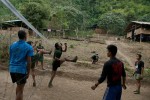 Medical staff and students of the Free Burma Ranger's Jungle School of Medicine Kathoolei play a competitive game of Takraw in camp. Takraw is a skill ball game that requires each team to pass the ball over the net and within the court boundaries using only their heads and feet, touching the ball a maximum of three times on each play. The team who fails this, gives up a point and each game is played to 15 points. (From left to right) The camps outpatient clinic, classroom and women's dormitory line the hillside. 