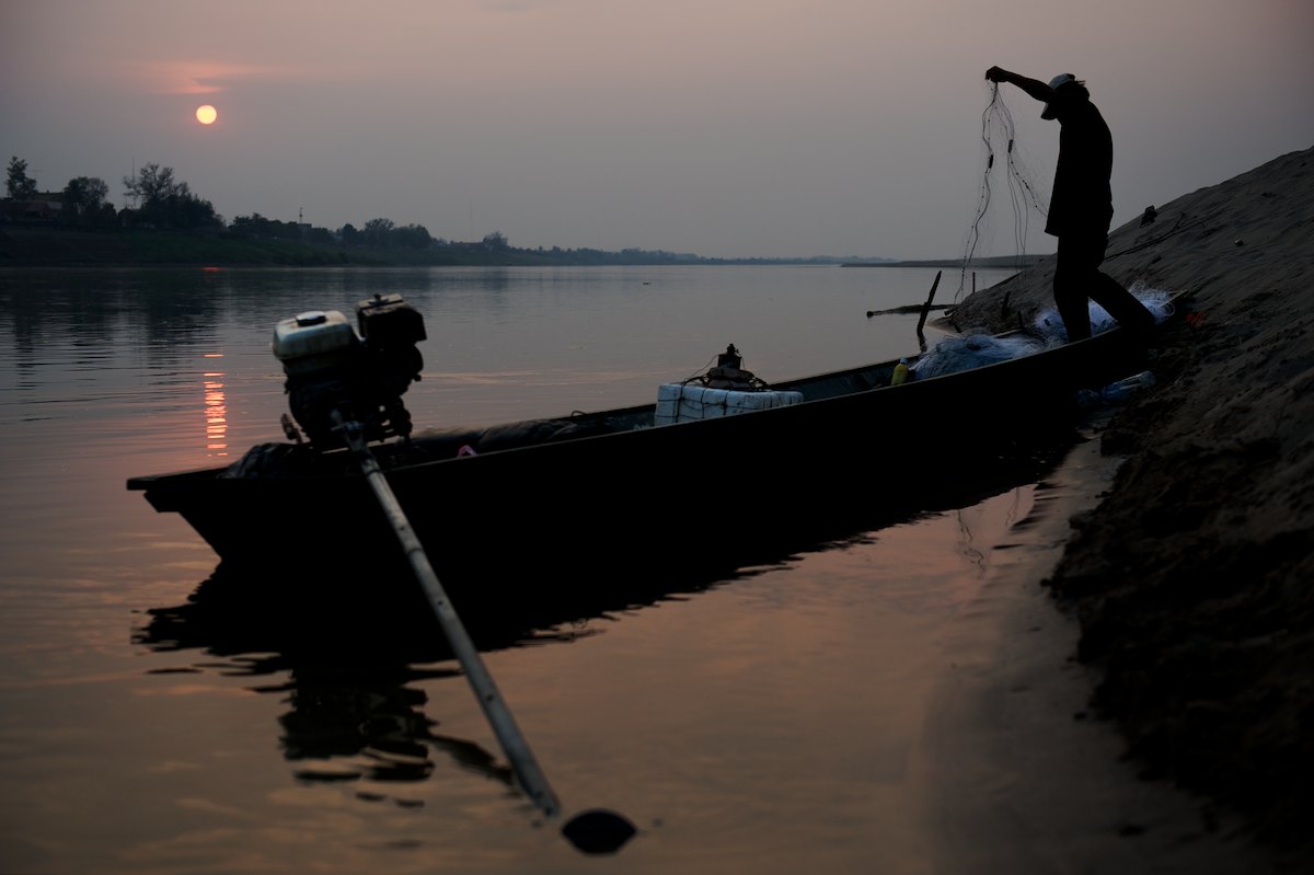 As night falls, a Laotian fisherman prepares to set his nets across the Mekong River.