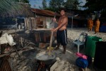 Chan boils sea cucumber outside his home. Prior to boiling, the night's sea cucumber catch is rinsed, gutted and cleaned using large plastic drums. Once boiled, the sea cucumber will be laid out over corrugated metal to dry in the sun and over a low fire.