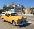 Photo of Cuban youth driving a yellow, vintage Pontiac on the Malecon Drive in Havana, Cuba. 