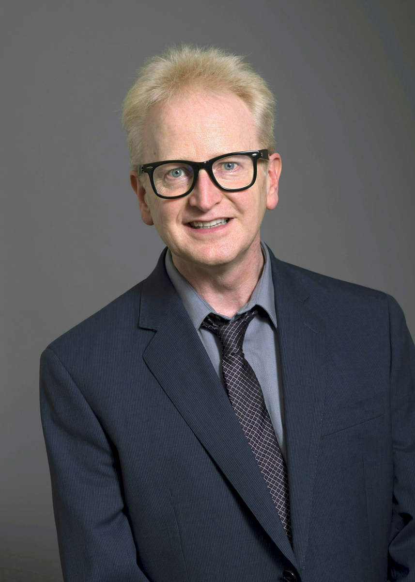 A studio portrait of a professor at Emerson College with a gray background.