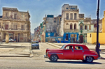 Photo of a classic old red car going down the Malećon Drive in Havana, Cuba showing desolate buildings in the background.