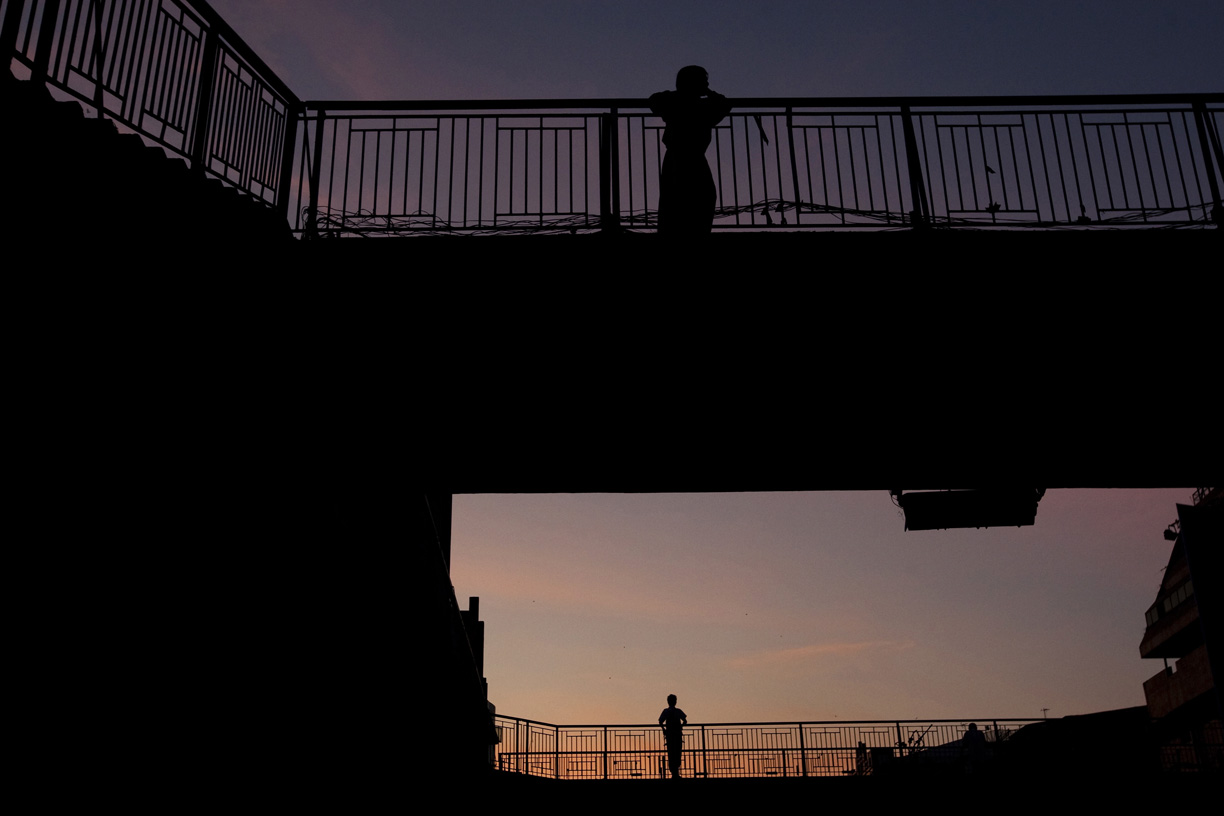 Men stand on a pedestrian overpass at dusk.