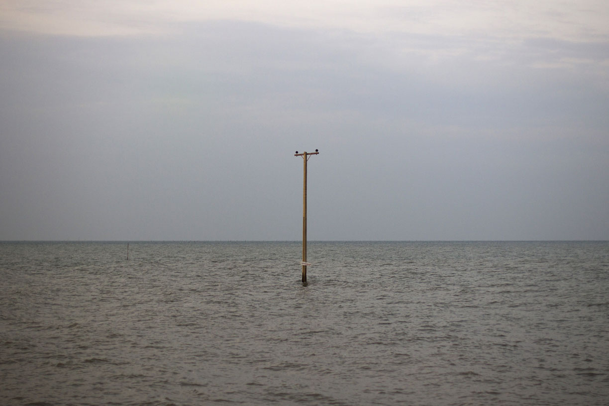 As a consequence of rising sea levels, an electrical power line pole stands in the sea where a village once stood near Wat Khun Samut Chin, Thailand.