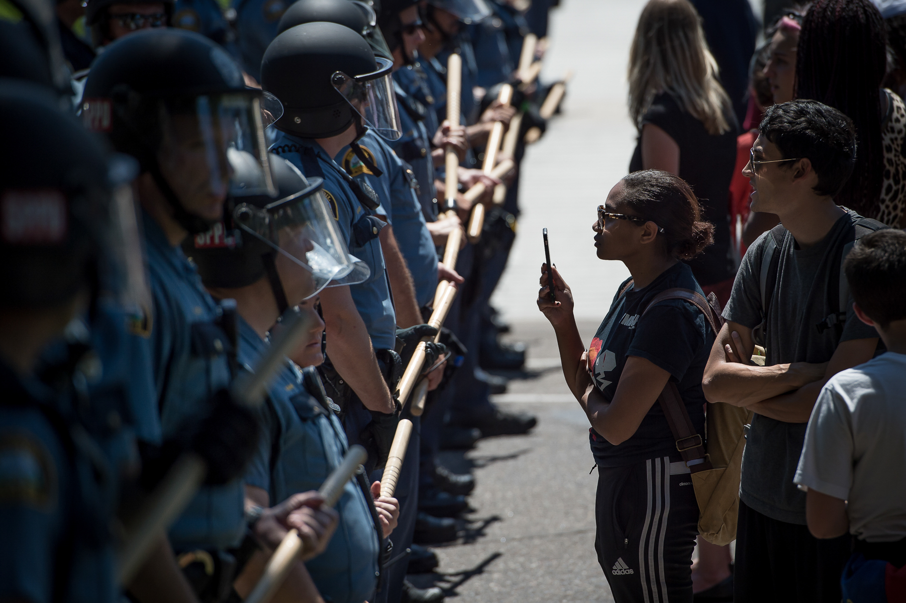 Equipped with just her phone, a protester documents a standoff between police and protesters after law enforcement removed protesters from an encampment outside the Governor’s mansion in St. Paul, MN on July 26, 2016. On July 6, 2016, Philando Castile was killed by a police officer during a traffic stop in St. Paul, MN. For over two weeks, community members held rallies and occupied the space outside the Governor’s mansion in protest of another police killing of a black man. On July 26, law enforcement removed the protesters from the occupation.