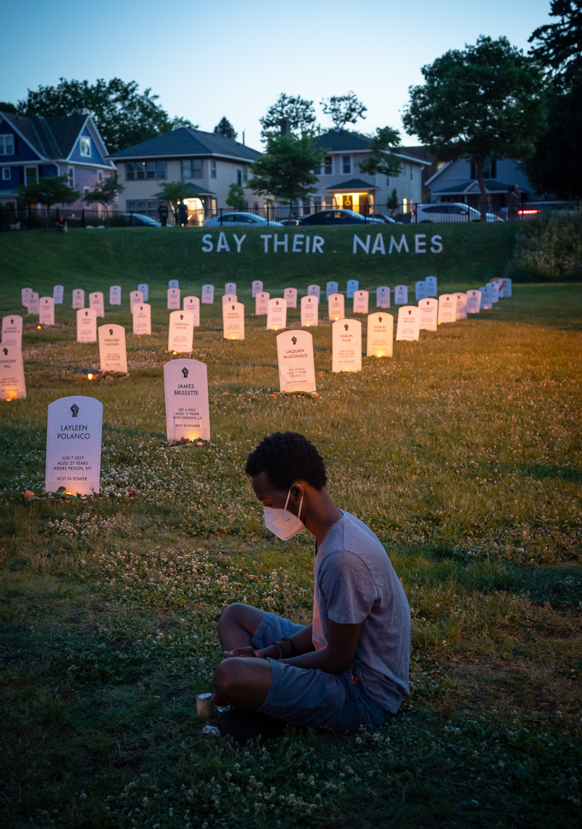 MINNEAPOLIS, MN / JUNE 7, 2020:  A young man sits quietly as community members gather at the Say Their Names Cemetery in Minneapolis on June 7, 2020, for a candlelight vigil to honor George Floyd, and others who have been killed by law enforcement in this country. The killing of George Floyd by Minneapolis police officer Derek Chauvin on May 25, 2020 ignited nationwide protests against racism and police brutality. In response to his death, the Say Their Names Cemetery art  installation was created by University of Pennsylvania students Anna Barber and Connor Wright, and has drawn visitors from all around the world.