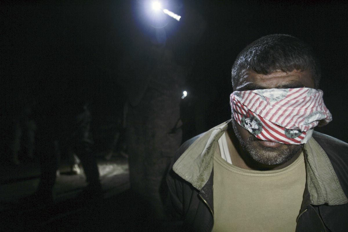 A blindfolded man is held at gunpoint by U.S. army soldiers from Blackfoot Company, 2nd Battalion, 23rd Infantry Regiment, while they conduct a night raid, Diyala province, Iraq, 2007.