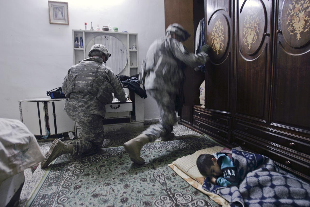 A boy sleeps in his home as U.S. army soldiers from Blackhawk Company, 1st Battalion, 23rd Infantry Regiment, search his room, Baghdad, Iraq, 2007. 