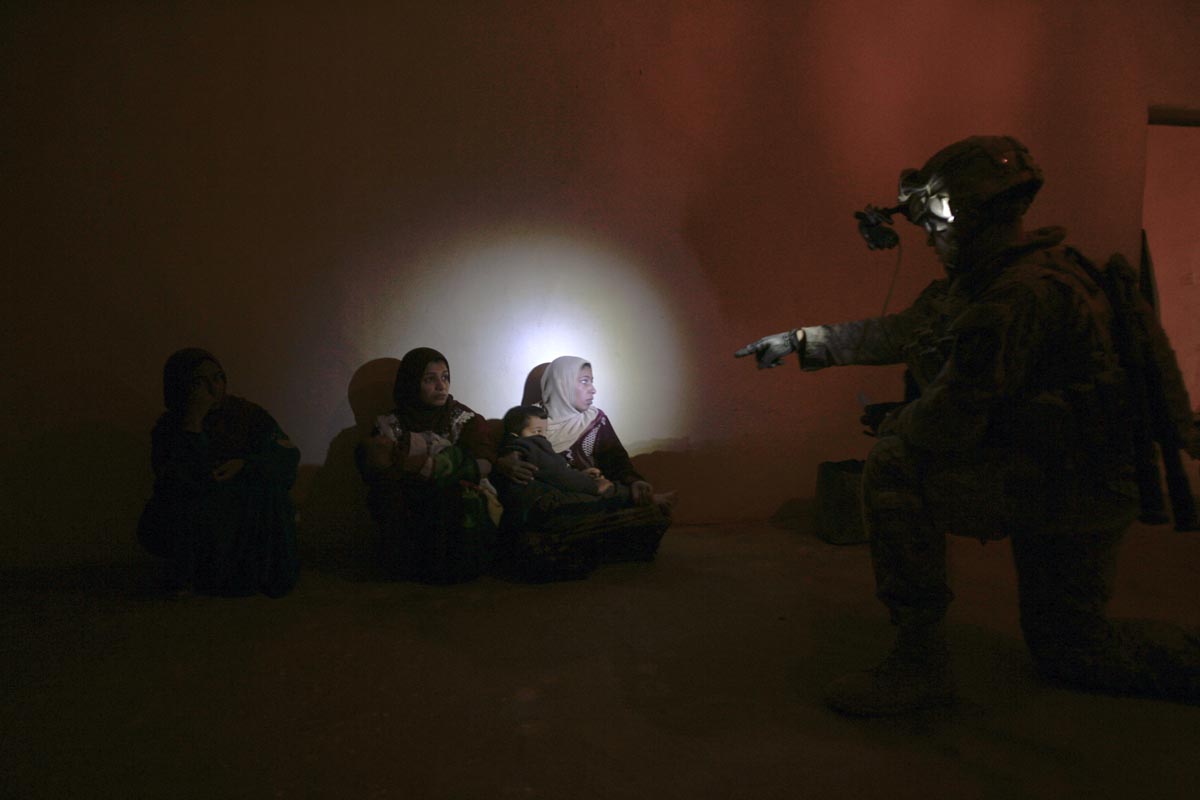 A U.S. army soldier from Blackfoot Company, 2nd Battalion, 23rd Infantry Regiment, interrogates a family in their home during a night raid, Diyala province, Iraq, 2007.
