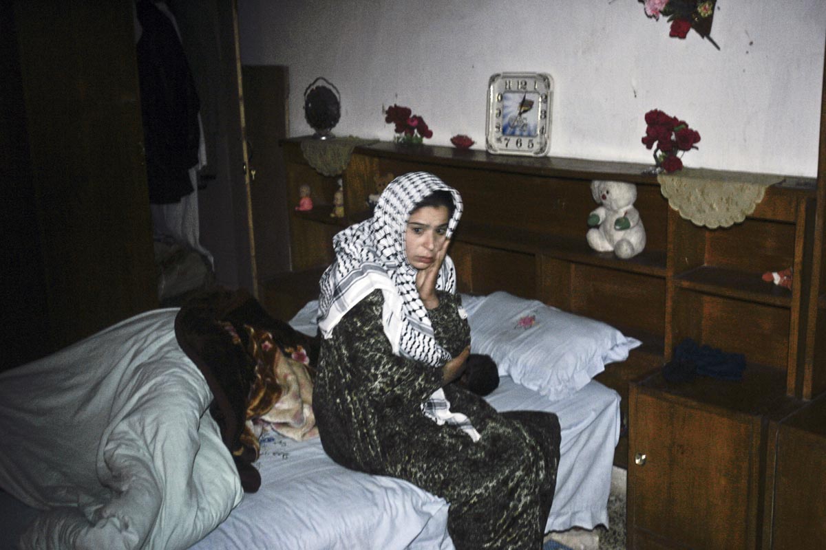 A woman sits stunned in her bedroom, as U.S. army soldiers from Blackfoot Company, 2nd Battalion, 23rd Infantry Regiment, search her home and detain her husband during a night raid, Diyala province, Iraq, 2007.