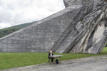 A souvenir seller waits for customers as she sits next to a monument to the WWII Battle of the Sutjeska, Tjentiste, Bosnia and Herzegovina, June 17, 2017. Thousands of monuments of all shapes and sizes were erected in Yugoslavia throughout the 1960's and 1970's to commemorate important historical events and WWII battles. A large number of the monuments were heavily damaged or destroyed on purpose in the 1990's conflicts. Those that survived are still visited by Yugoslavs and people who feel nostalgia for the old country. 