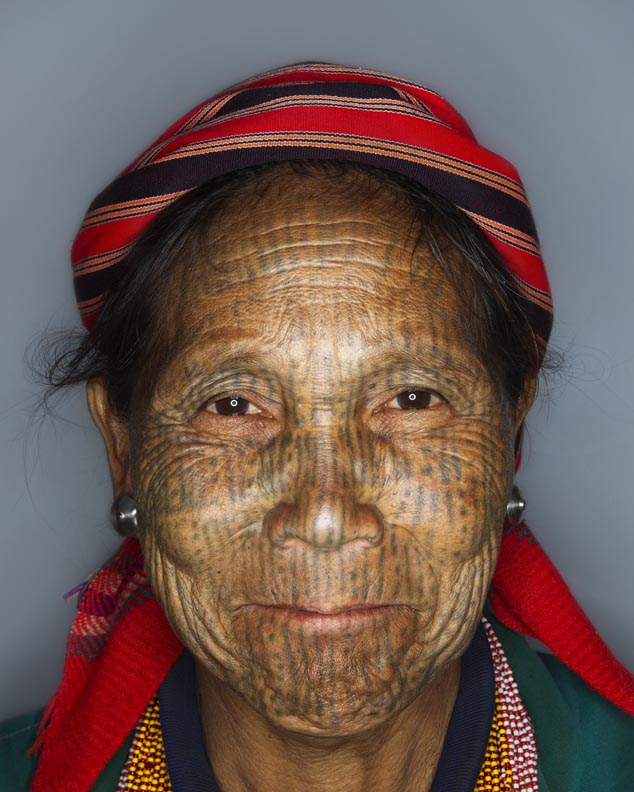 Awe Phan, age 53, poses for a photo in Myanmar's Chin State. The sparsely populated Chin State is home several subgroups all calling themselves Zo-mi meaning 'mountain people.' Separated from the rest of Myanmar (formerly Burma) by mountains and being a travel restricted State for foreigners, the Chin have little contact with the modern world. Historically the Chin were adored for their beauty and King's would come to villages to steal men's wives. As a measure against their women being stolen, village elders started tattooing teenage girls to make them 'ugly'. The tradition stuck and over generations eventually lost it's original meaning of ugliness and came to represent courage, beauty and strength. However, as these traditional groups began moving outside their villages, the struggle between tradition and modernity has placed tribal Chin culture under increasing threat of being absorbed by the dominant Burmese. Unique language, customs and dress have been abandoned. Under this pressure to assimilate, the practice of facial tattooing has also been discontinued. Currently there remain only a handful of women adorning facial tattoos.