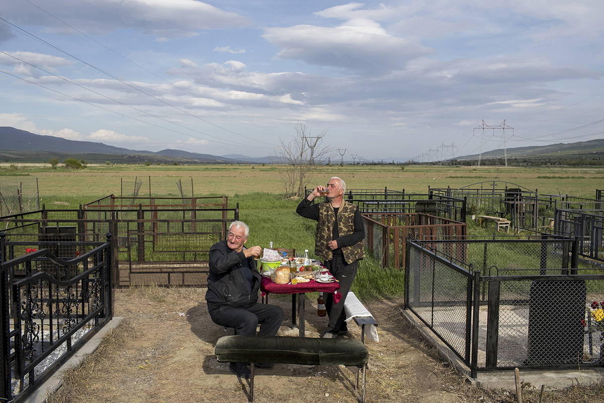An Ossetian person (L) and a Georgian person (R) pay respects to a deceased relative of theirs, as they have a drink together at a cemetery in the village of Khurvaleti, Georgia, April 29, 2019.       