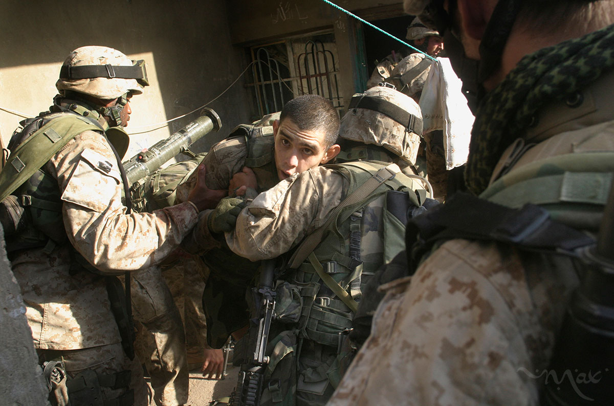 Marines help Lance Corporal Enrique Mayer who was shot in the leg after being ambushed by insurgents. After fleeing the ambush Mayer found shelter in the home behind him. Mayer lay bleeding as the firefight raged. After the insurgents were killed Mayer was lifted out of the house when he became dizzy because of his blood loss and fell on his fellow Marines.