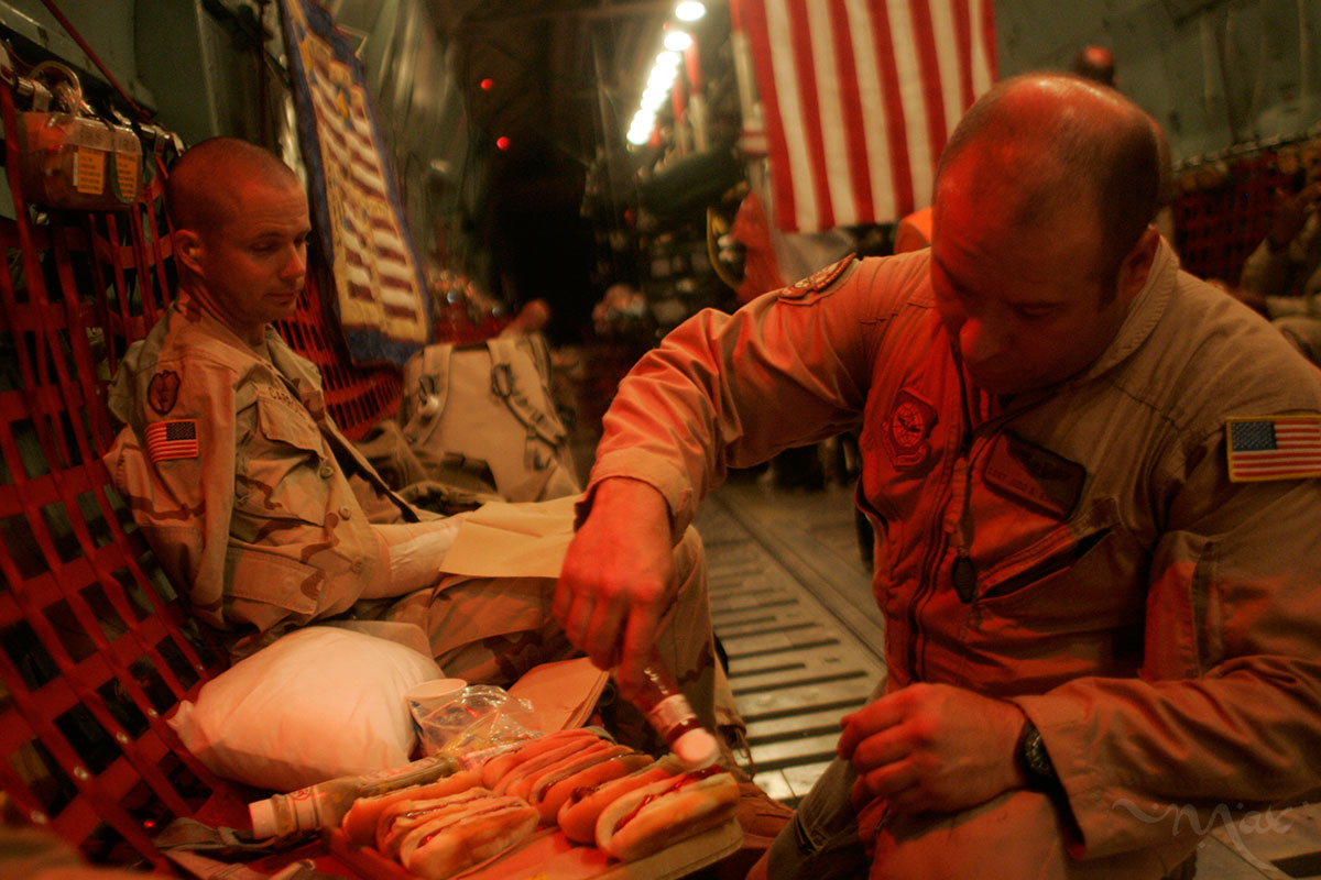 Flight medical technician, Staff Sergeant Judd Everly from the 94th Aeromedical Evacuation Squadron serves hot dogs to wounded soldier Staff Sergeant John Carroll, who has a broken hand, during the flight of a C-141 medical transport from Balad Air Base in central Iraq to Landstuhl  Regional Medical Center in Germany where he will receive treatment. The flight medics try to make sure the wounded have all of their medical and comfort needs taken care of during the flight. 
