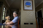 Kevin Bourgeois sits with his Norwich Terrier, Pippa, with a framed poster, from the papal visit of Pope John Paul II to New Orleans from 1987, seen behind him at his home in New Orleans, La. Tuesday, Aug. 6, 2019.