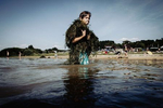 A boy covered with sea weed is walking out of the lake at the Krombachtalsperre in Germany