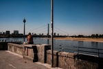 A bald man is sitting on a wall at the riverside of river Rhine in Duesseldorf in Germany in August 2022. On the other side of the river its dried out bank can be seen The photo is part of a reportage for Bloomberg about the drought along the Rhine. 