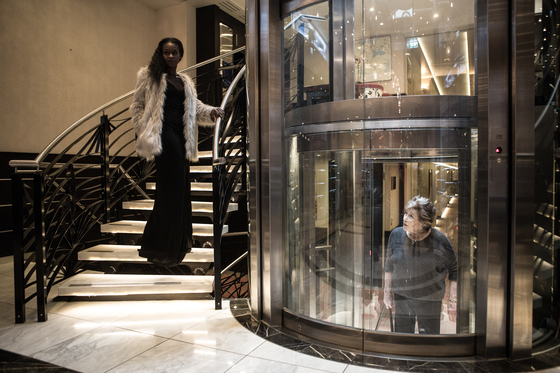 A model is walking down the stairy of a tourist river boat while another woman that is using a transparent elevator watches her