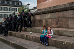 two little girls are sitting on the stairs leading to a monument and are eating icecream, Left to them a big group of police officers is standing