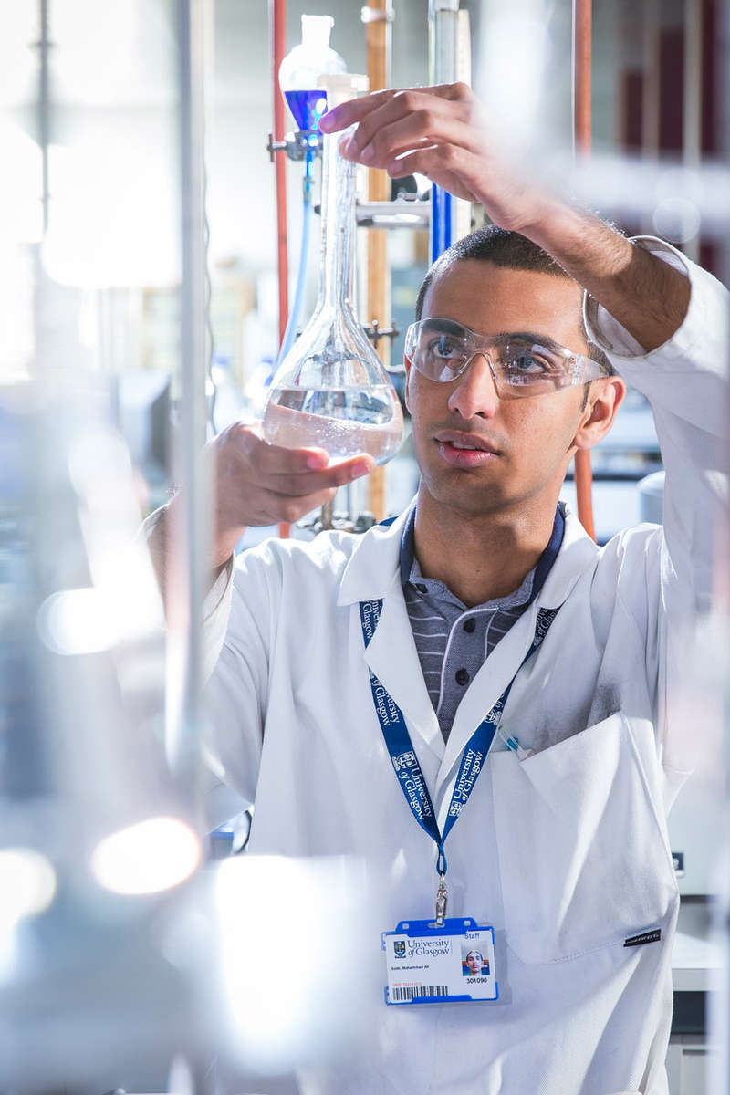 Environmental portrait of young apprentice scientist at work in a laboratory. Man looking at a test tube.