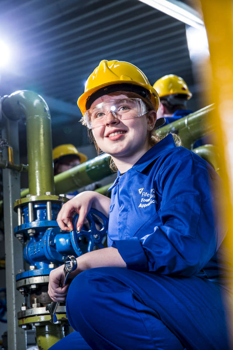 Environmental portrait of young apprentice at work. Woman with a hard hat in a factory