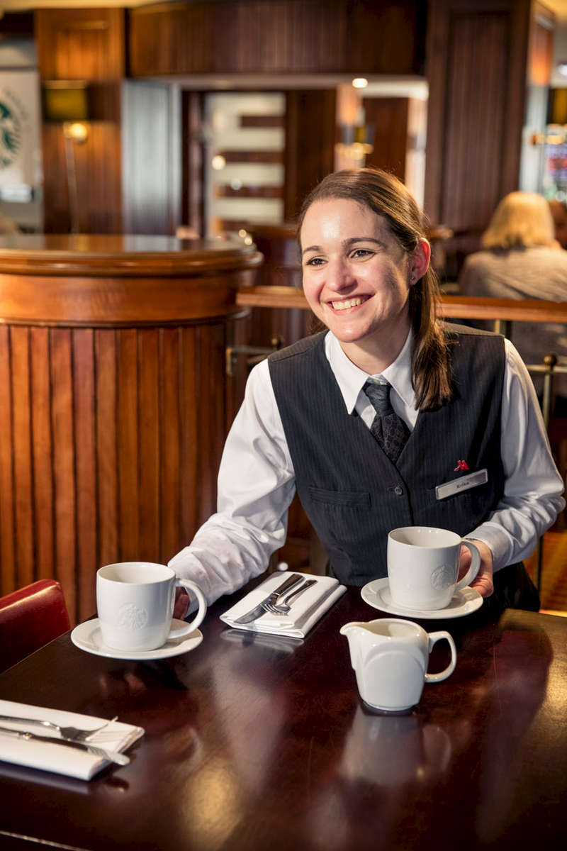 Environmental portrait of young apprentice waiter working in hospitality. woman serving coffee in a hotel.