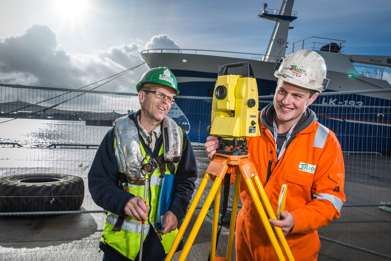 Environmental portrait of young apprentice at work with a theodolite at a harbour pier. young man with a mentor. 