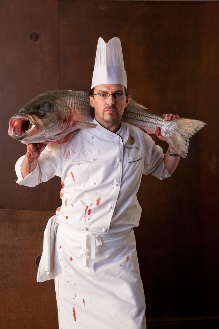 a chef in whites holds a giant bloody fish around his shoulders.
