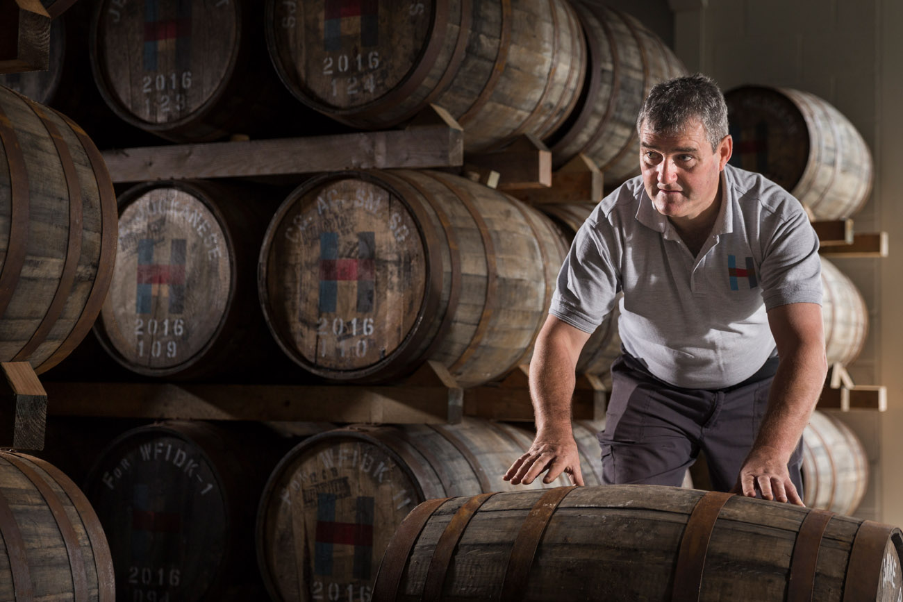 man rolling a cask of whisky in a warehouse.