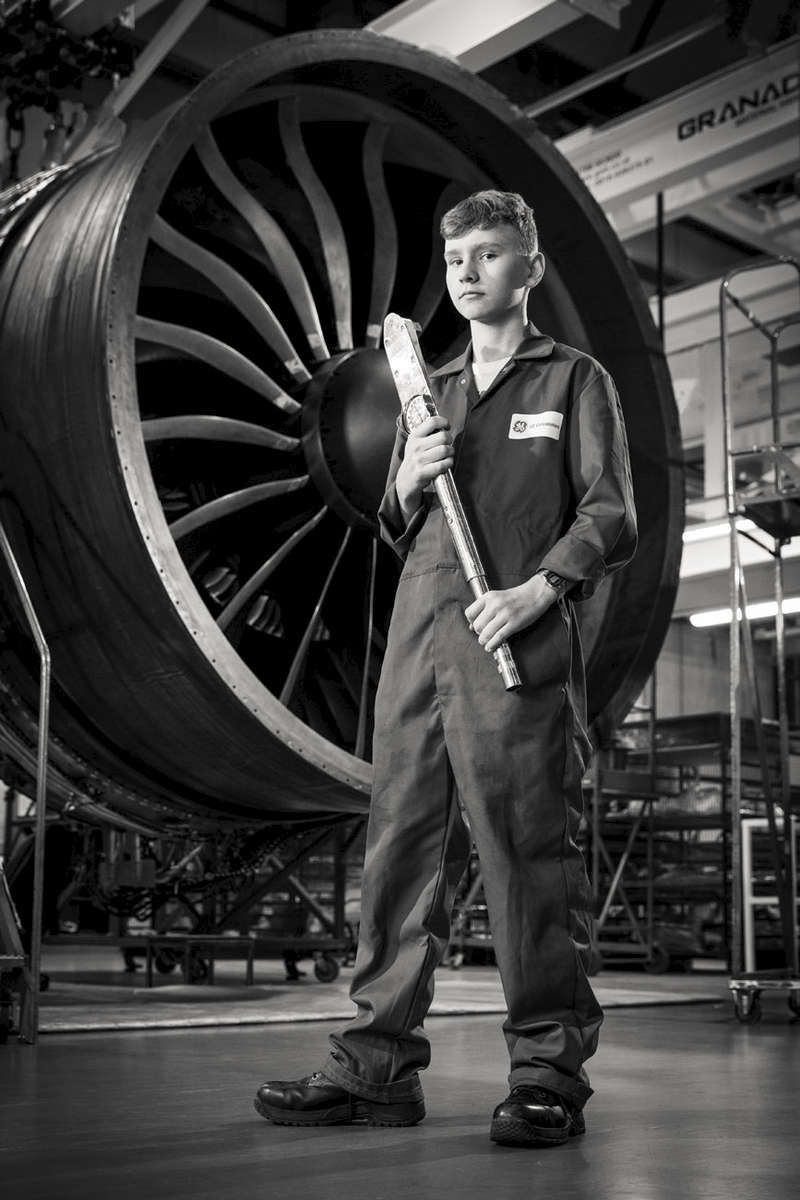 Environmental black and white portrait of young aviation apprentice in front of a jet engine at BAE systems.