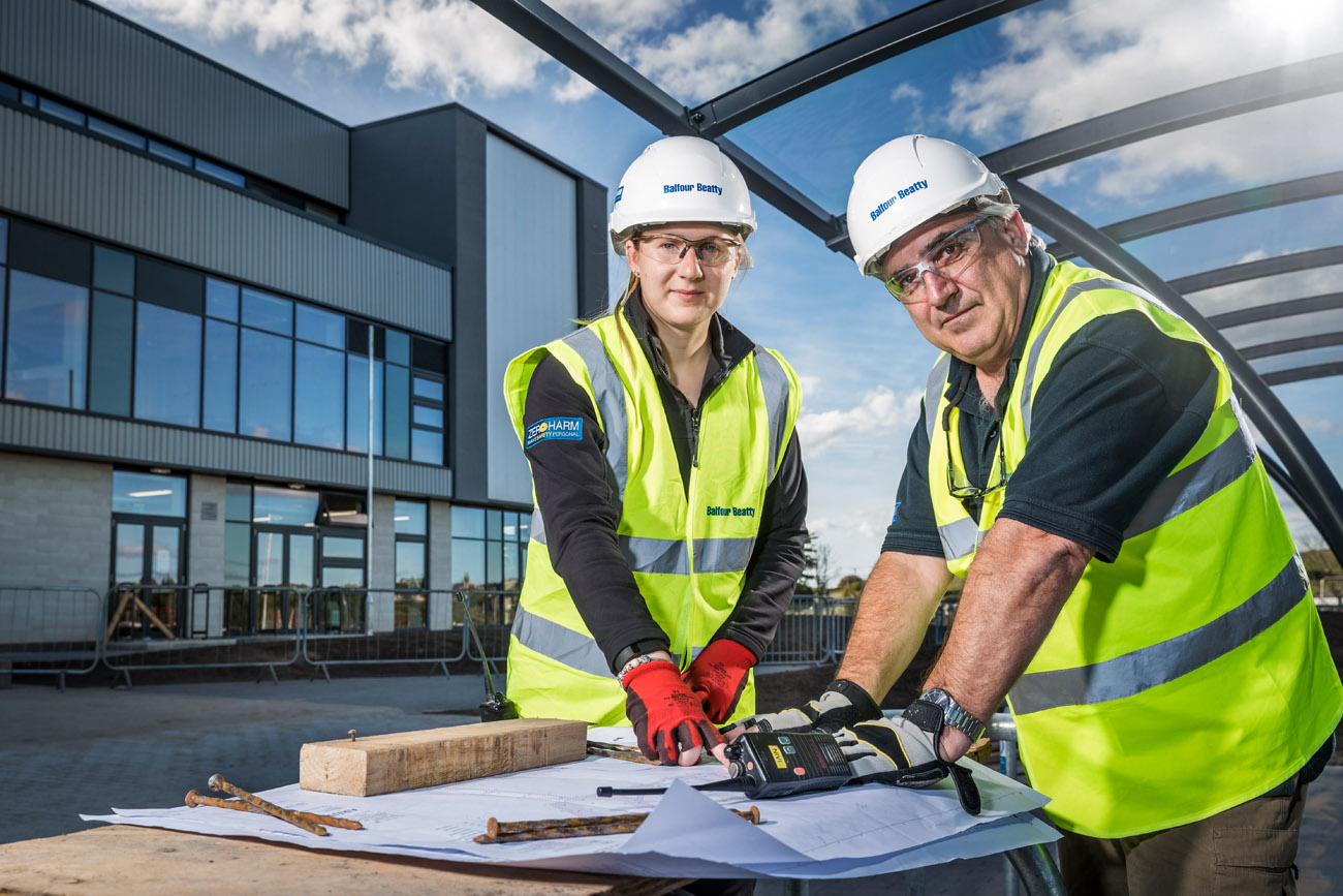 Environmental portrait of young apprentice with mentor at work with building plans