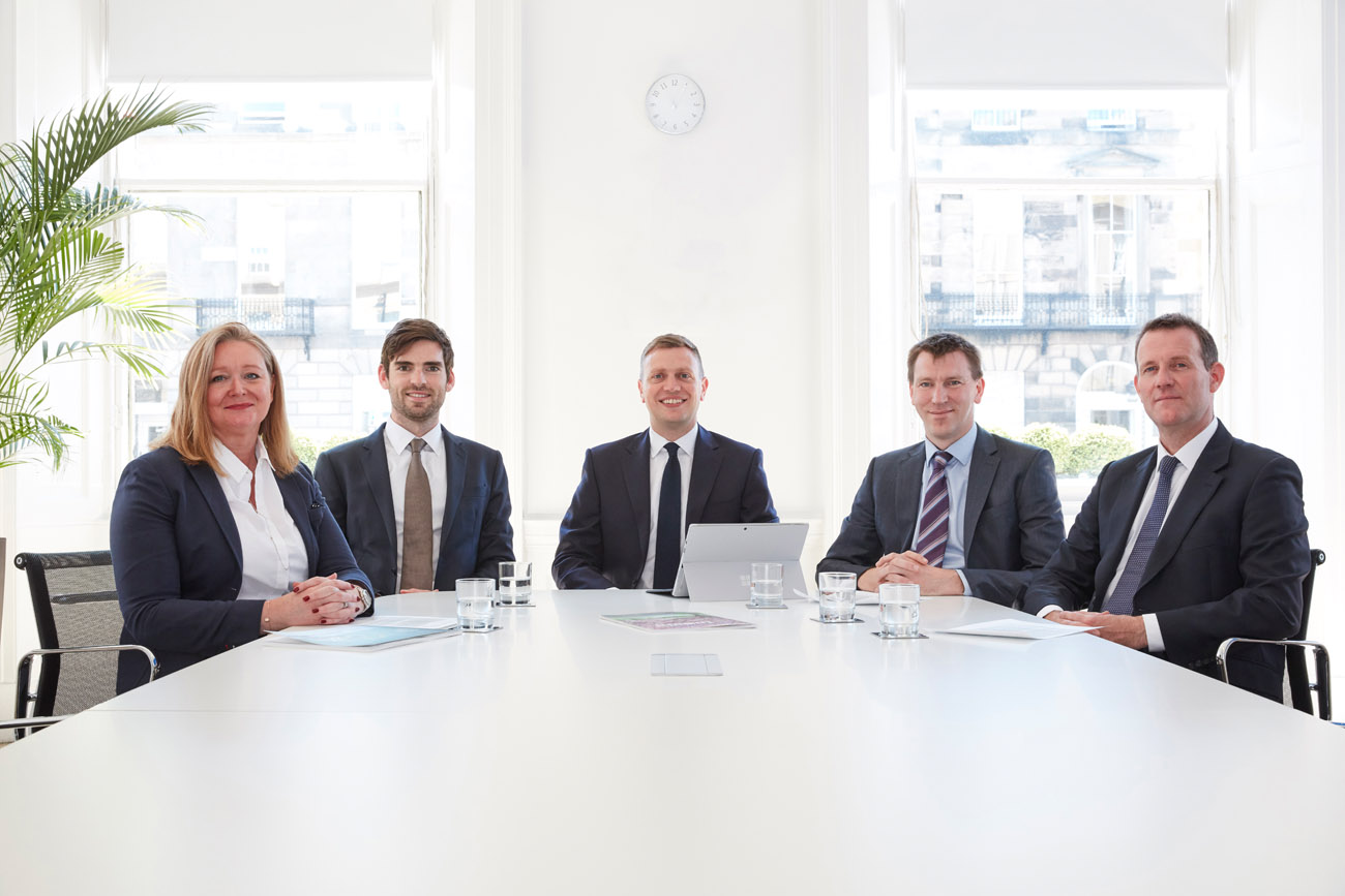Corporate group portrait of people in an office sitting around a desk.