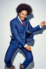 High energy studio fashion portrait of a black man in a blue suit leaping in the air