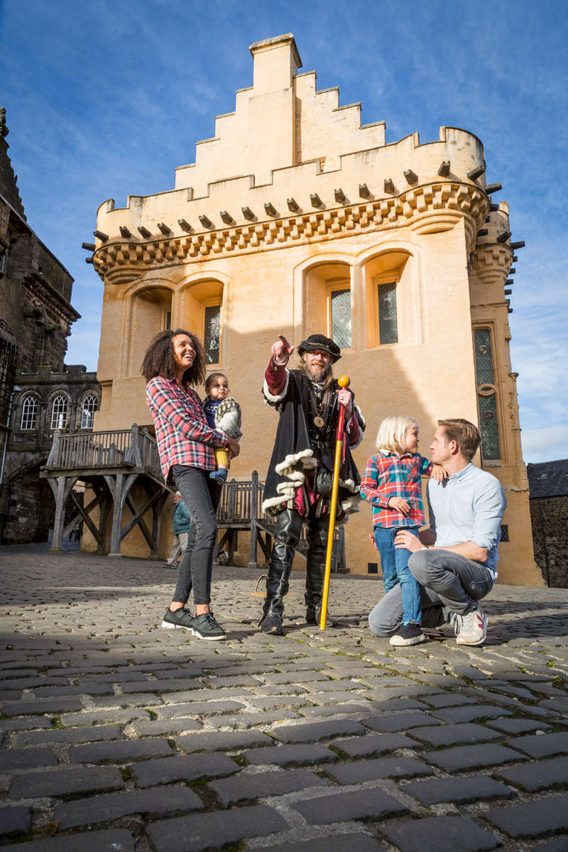 Historic Scotland  - family being shown around Stirling Castle courtyard in the sun by a guide in period dress