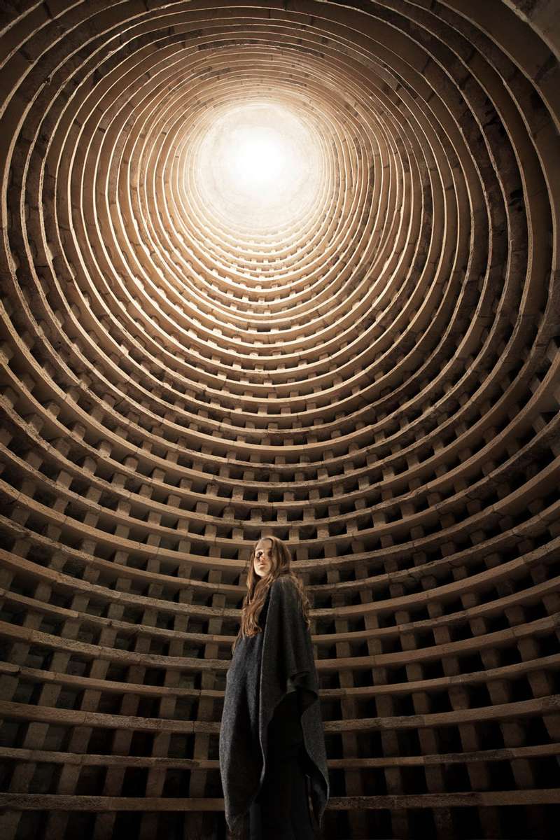 a girl stands inside a surreal round building with a bright light above. girl inside a dovecot 