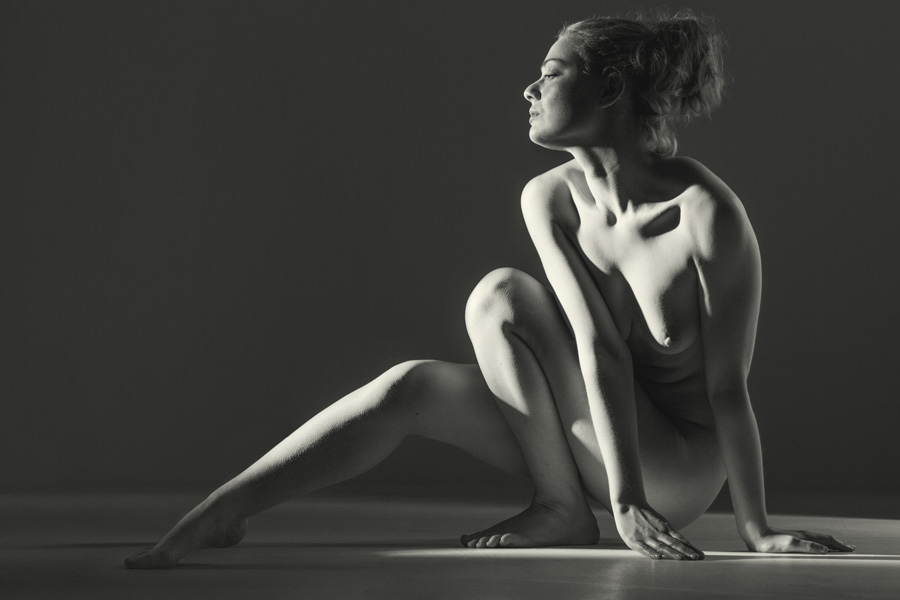 seated nude girl in low light in a dark studio. Fine art beautiful naked woman sitting