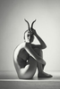 seated nude woman in a studio holding horns to her forehead