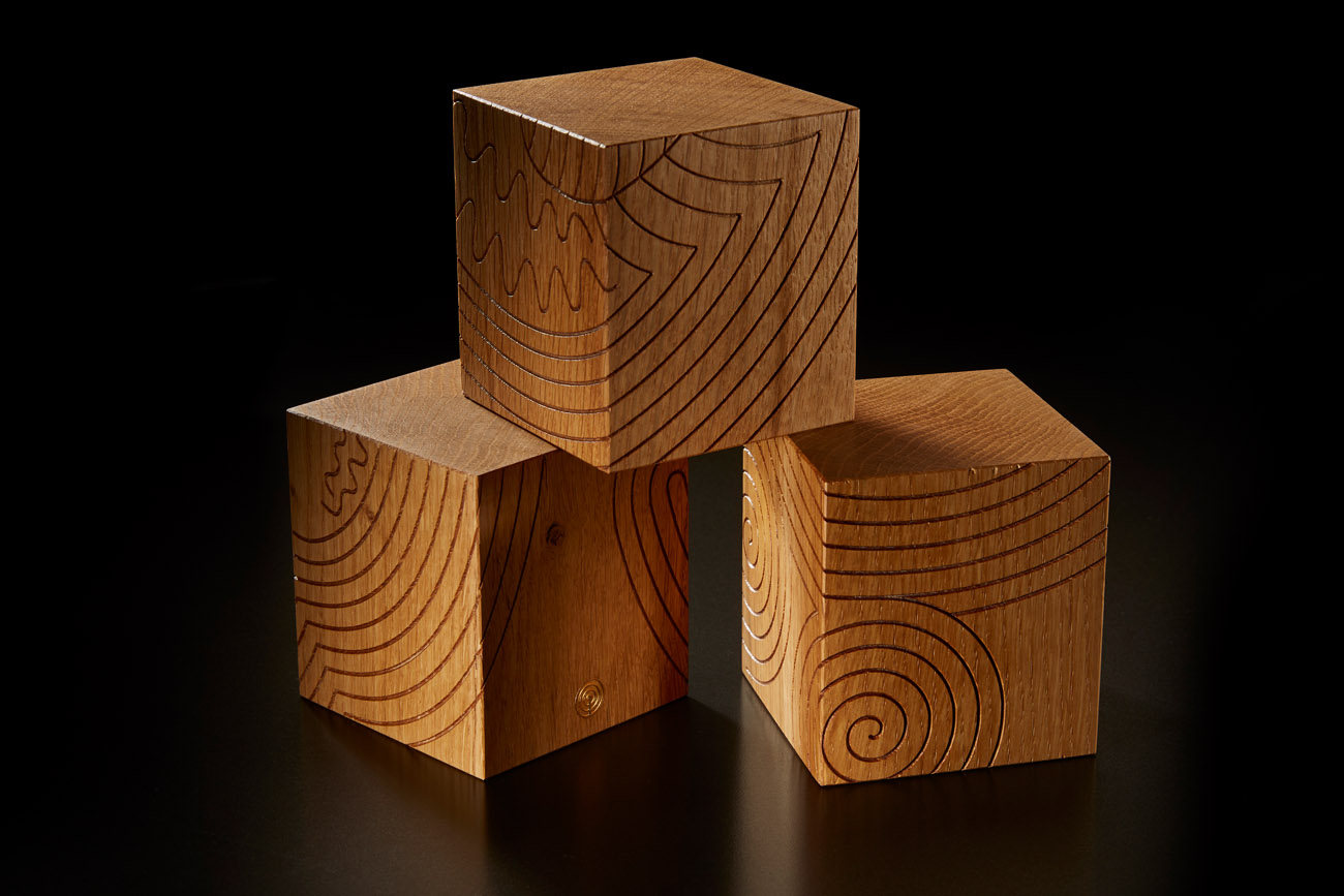 finely crafted bespoke  wooden cubes with celtic designs stacked in a studio on a black background