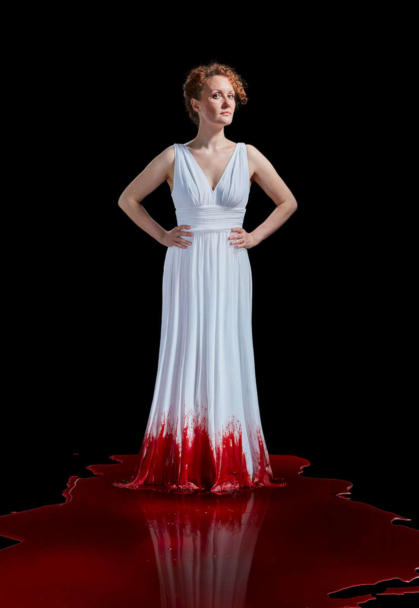 woman in a long white dress with blood on it while standing in a pool of blood 