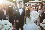 A happy bride and groom are captured in a candid moment after their wedding ceremony at Silver Creek Valley Country Club in San Jose, California. The bride is wearing a stunning white wedding dress with a flowing train and holding a bouquet of flowers, while the groom is dressed in a sharp black suit with a white shirt and tie. The couple is standing on a lush green lawn, with trees and a blue sky in the background. The bride is leaning into the groom, with a big smile on her face, while the groom is looking directly at the camera with a relaxed expression. This image captures the joy and excitement of a newlywed couple on their wedding day, as well as the elegant surroundings of a country club wedding venue.
