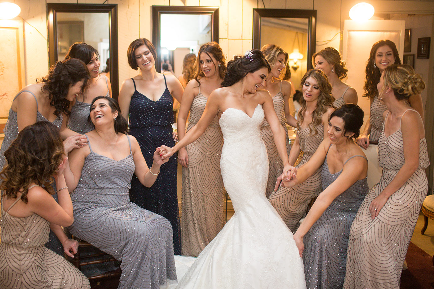 The image shows the bride and her bridesmaids getting ready for the wedding in the Chapel at the Union Hill Inn in Sonora, California. The women are standing together in the chapel, which features wooden beams, stained glass windows, and a rustic chandelier. The bride is wearing an elegant white gown, while the bridesmaids are dressed in matching burgundy dresses. They are all smiling and appear to be excited as they prepare for the wedding. The image showcases the beauty of the venue and captures the joyous atmosphere of the occasion.
