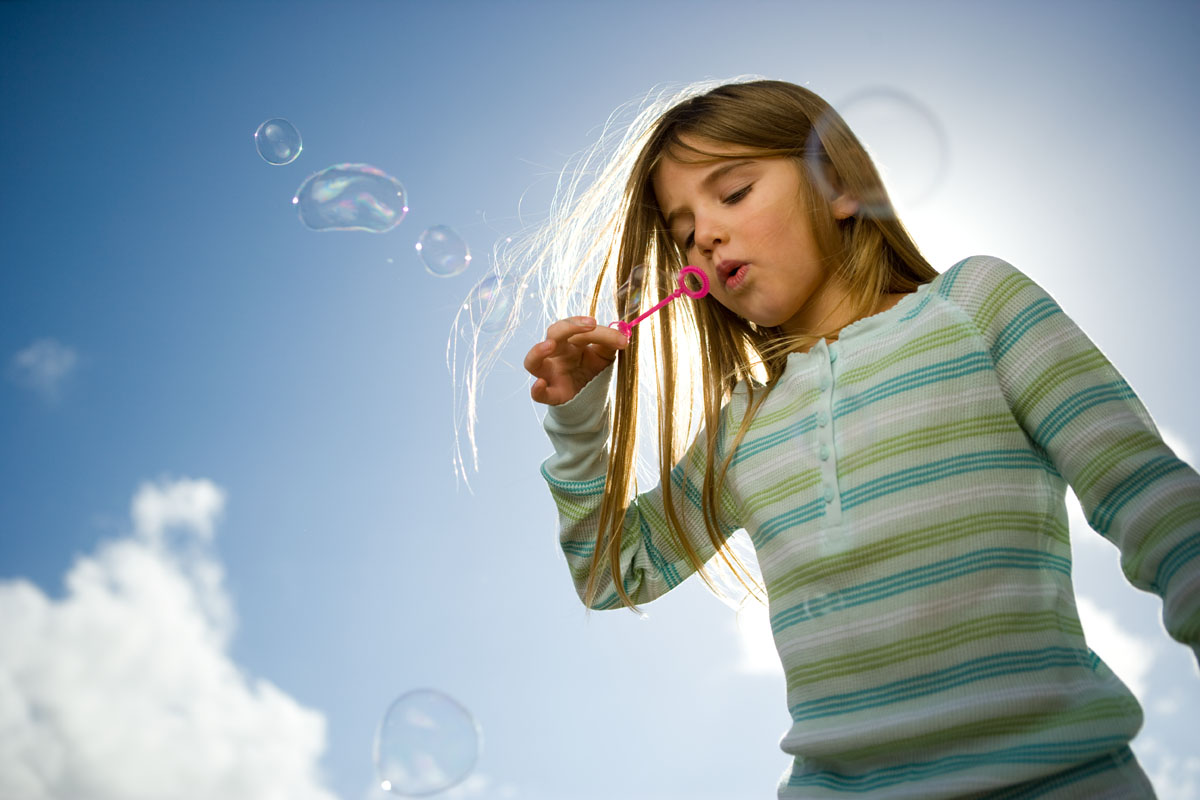 Young girl with a striped shirt blowing bubbles with a blue sky behind her shot for Stericycle ad campaigns.