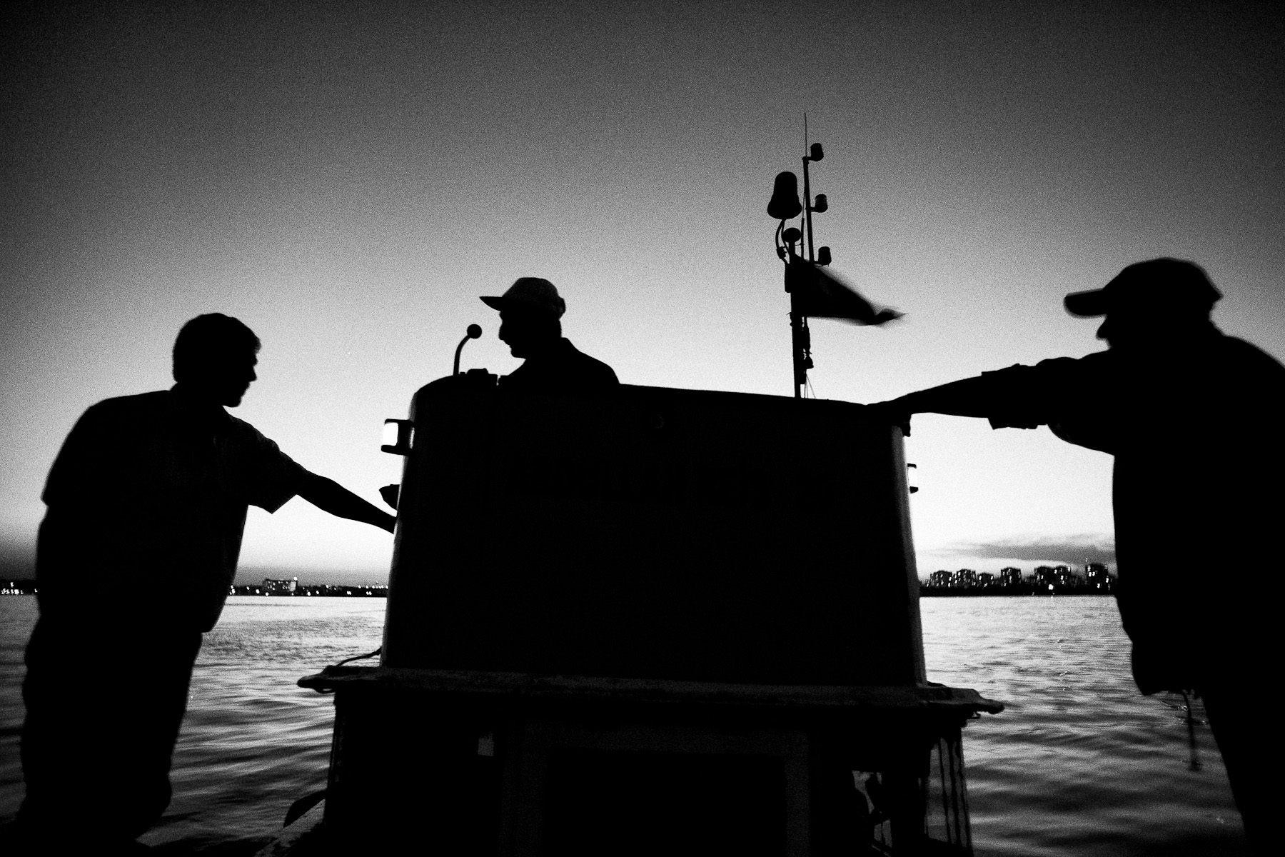 Waiting for the night to fall completely and the fish to come in, Cevat, Adem and Cinar, discuss the tactics. A lot of work over night is coordinated with their friend's boat that only has two fishermen on board.