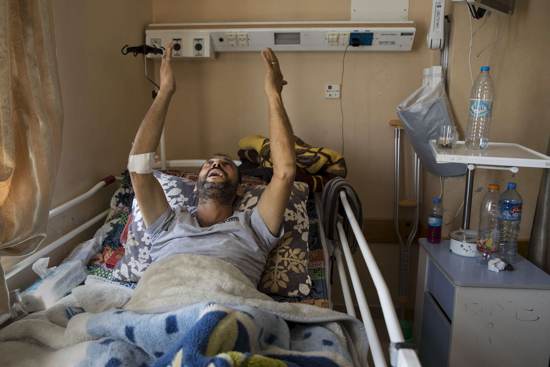 GAZA CITY, GAZA STRIP- MAY 20,2018: A patient prays for his pain to be relieved from his bed at the Al Shifa hospital on May 20, 2018 in Gaza Strip. According to the International Committee of the Red Cross (ICRC), 13,000 Palestinians were wounded (as of June 19, 2018), the majority severely, with some 1,400 struck by three to five bullets. No Israelis were physically harmed during this time period, Israel's use of deadly force was condemned during the UN general assembly on June 13 th along with other human rights organizations.The Israeli military (IDF) started using new weaponry, explosive bullets that shatter bones, tissue, destroying veins and arteries, the aim is to create a handicapped community, especially amongst the young male population. Many of the wounded protesters have to undergo multiple surgeries to try to save their limbs, and in some cases amputation is the only solution. With limited healthcare available in Gaza many were sent to Jordan and Turkey for further treatment. More issues that plague Gaza include a water supply that is 95 percent contaminated and a population forced to live without electricity for 21 hours a day. Gaza is compared to Venezuela with almost half of it’s labor force unemployed. Everyone is well aware that Gaza's two million inhabitants are trapped in a cycle of violence and poverty, living in an open air prison. The problems and complications affecting Gaza today are overwhelming. The world, seemingly accustomed to the suffering of the Gazan people turns a blind eye. (Photo by Paula Bronstein ) 