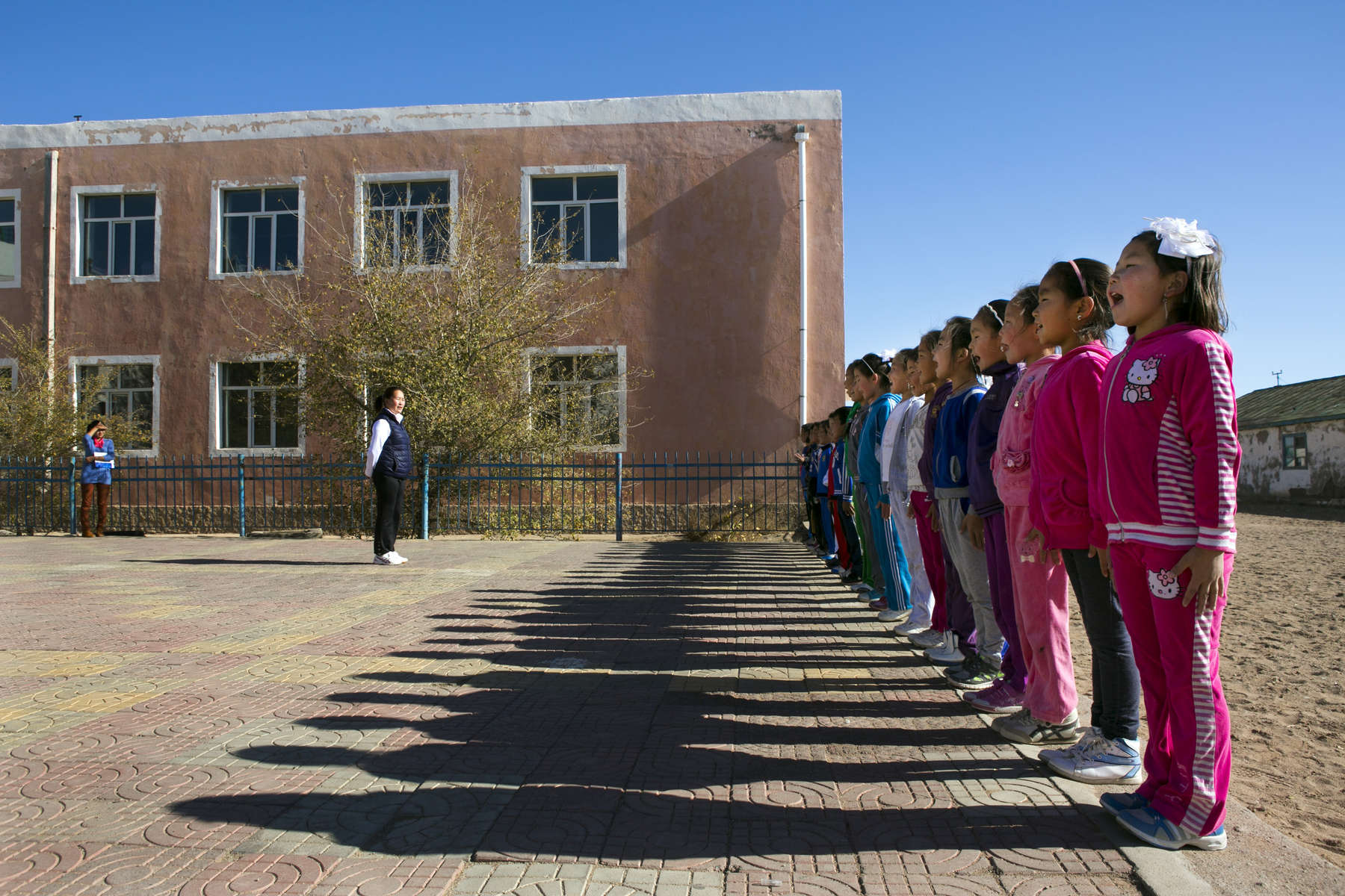KHANBOGD-SOUTH GOBI DESERT, MONGOLIA - OCTOBER 13:  Students line up during a physical education program at the Khanbogd Secondary school October 13, 2012  in Khanbogd, Mongolia. The population of Khanbogd has doubled in the last few years along with the secondary school adding a new extension to accommodate the growing number of students since Oyu Tolgoi employs most of the people in the town.The Oyu Tolgoi copper and gold mine (translated means Turquiose Hill) is a combined open pit and underground mining project.  While the construction continues open pit mining is currently underway with full production expected later in 2012. When the mine starts full operation the country will be set to become one of the world's top copper and gold producers with estimates of 450,000 tons of copper and 330,000 ounces of gold. Financing for the project has come in part from the Rio Tinto Group and an investment agreement between Ivanhoe Mines and the government of Mongolia. Mongolia’s largest foreign investment project to date which is projected to add one-third of future value to the country’s GDP. Many estimate Mongolia to be the world's fastest growing economy with an estimated $1.3 trillion in untapped mineral resources. (Photo by Paula Bronstein/Getty Images)