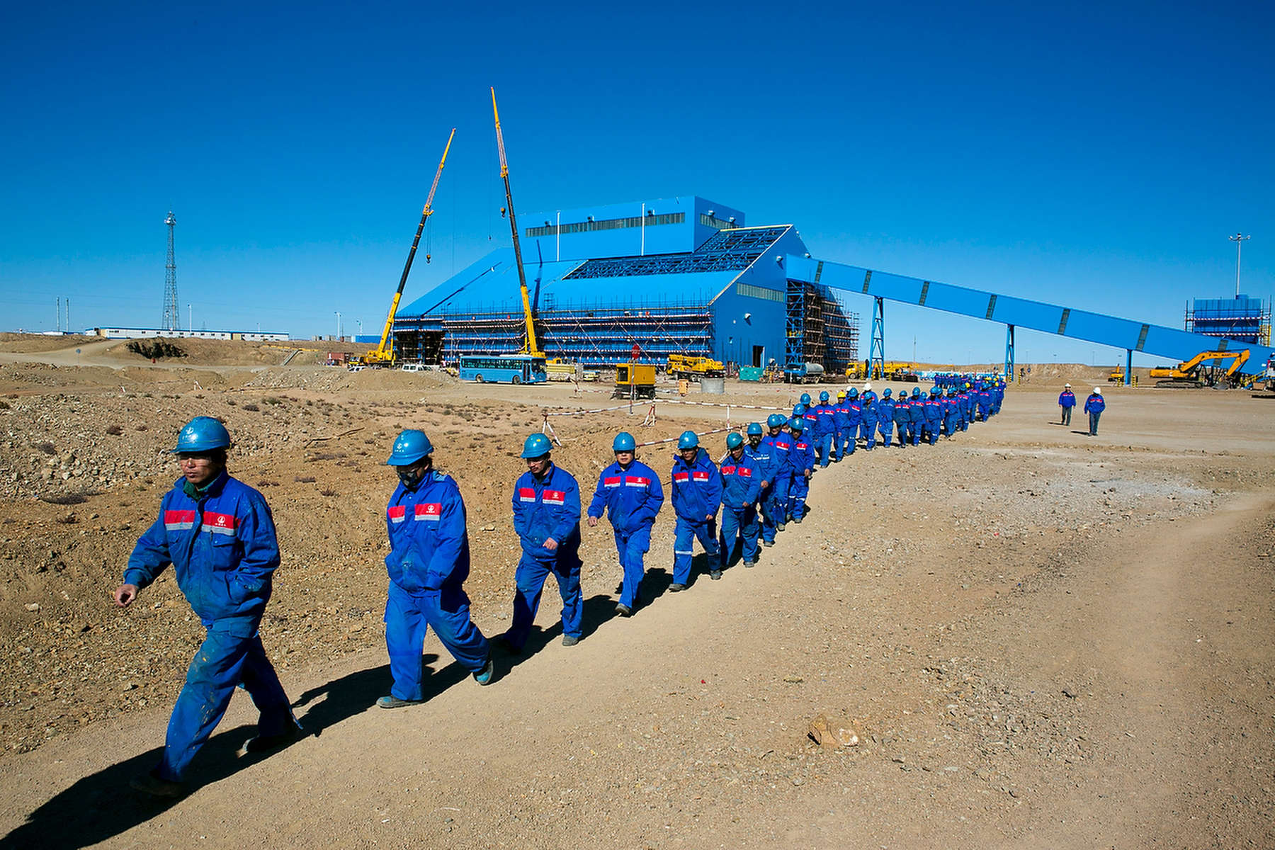 KHANBOGD-SOUTH GOBI DESERT, MONGOLIA - OCTOBER 11:  Chinese construction workers  march together as they leave on a lunch break at the Oyu Tolgoi mine October 11, 2012 located in the south Gobi desert, Khanbogd region, Mongolia. About 2,500  Chinese workers are contracted to help with construction onsite. The Oyu Tolgoi copper and gold mine (translated means Turquiose Hill) is a combined open pit and underground mining project.  While the construction continues open pit mining is currently underway with full production expected later in 2012. When the mine starts full operation the country will be set to become one of the world's top copper and gold producers with estimates of 450,000 tons of copper and 330,000 ounces of gold. Financing for the project has come in part from the Rio Tinto Group and an investment agreement between Ivanhoe Mines and the government of Mongolia. Mongolia’s largest foreign investment project to date is projected to increase the country’s GDP by 35%. Many estimate Mongolia to be the world's fastest growing economy with an estimated $1.3 trillion in untapped mineral resources. (Photo by Paula Bronstein/Getty Images)
