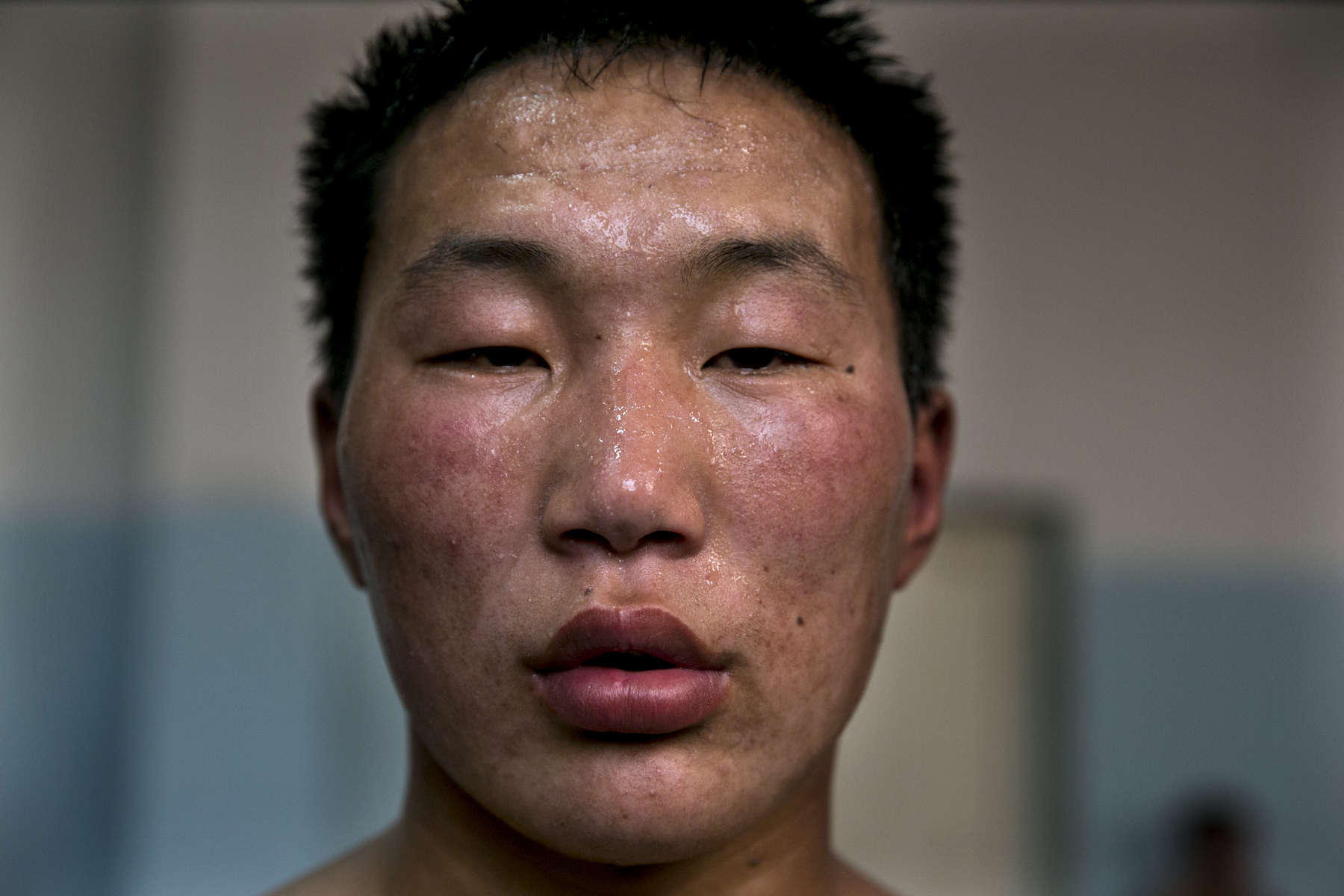 A Mongolian wrestler looks into a camera during a break in wrestling practice. Mongolia is the most sparsely populated country on earth, but its people are some of the strongest. In Mongolia, wrestling is the most important sport that runs deep into its culture along with horsemanship and archery. Going back for hundreds of years, history books tell the story of how Genghis Khan considered wrestling to be an important way to keep his army combat ready while back in the Qing Dynasty (1646–1911) regular wrestling events were held. In Mongolia’s capitol city, Ulan Batar is home to many wrestling schools where almost daily you can see dozens of young men sweating in crowded gyms while in schools both girls and boys are taught some wrestling techniques.While my photo story gives a real behind the scenes look, it is unusual for a woman to document this macho scene of sweat and endurance.