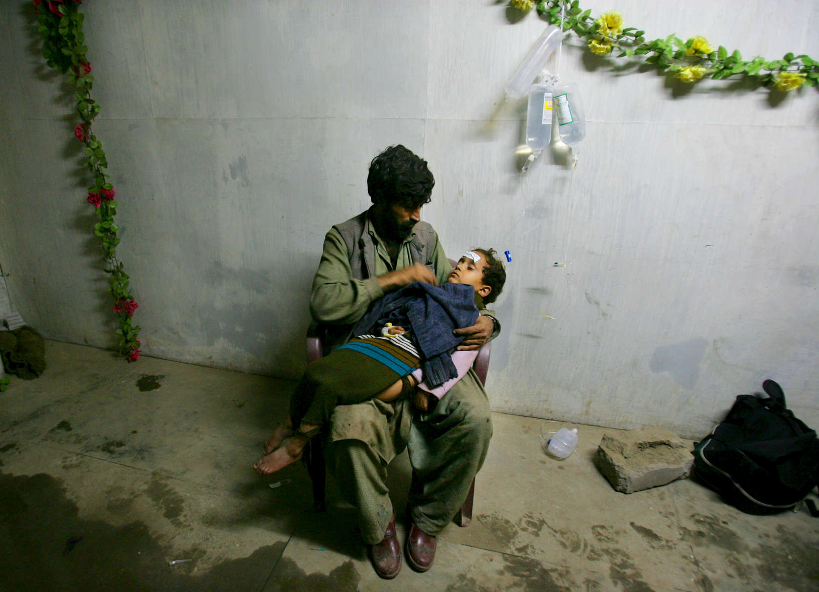 BALAKOT, PAKISTAN: A father holds his daughter  awaiting medical treatment at a makeshift trauma facility where earthquake survivors were brought in by helicopter from remote villages.  A devastating earthquake measuring 7.6 on the Richter scale hit northern Pakistan and neighboring India in early October leaving up to 3 million people homeless in Pakistan, killing almost 80,000 in Pakistan and another 1,400 in Indian-Kashmir. Rescue efforts were complicated by the remote mountainous landscape and the vast areas effected leaving the people in desperate situations. The injured were trapped for days with little food and no shelter as roads were blocked by landslides until helicopters were able to rescue the victims. Aid agencies could barely grasp the enormity of the natural disaster, the worst in Pakistan’s history. 